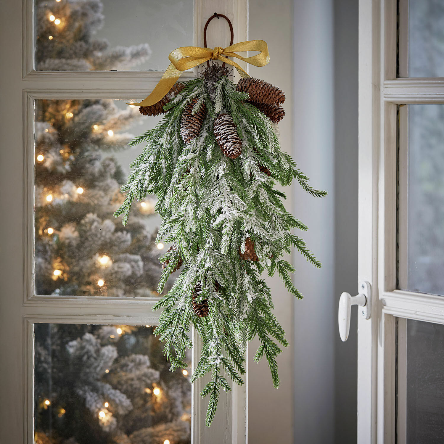 Décoration de Noël suspendue en branches vertes, pommes de pin enneigées et ruban doré