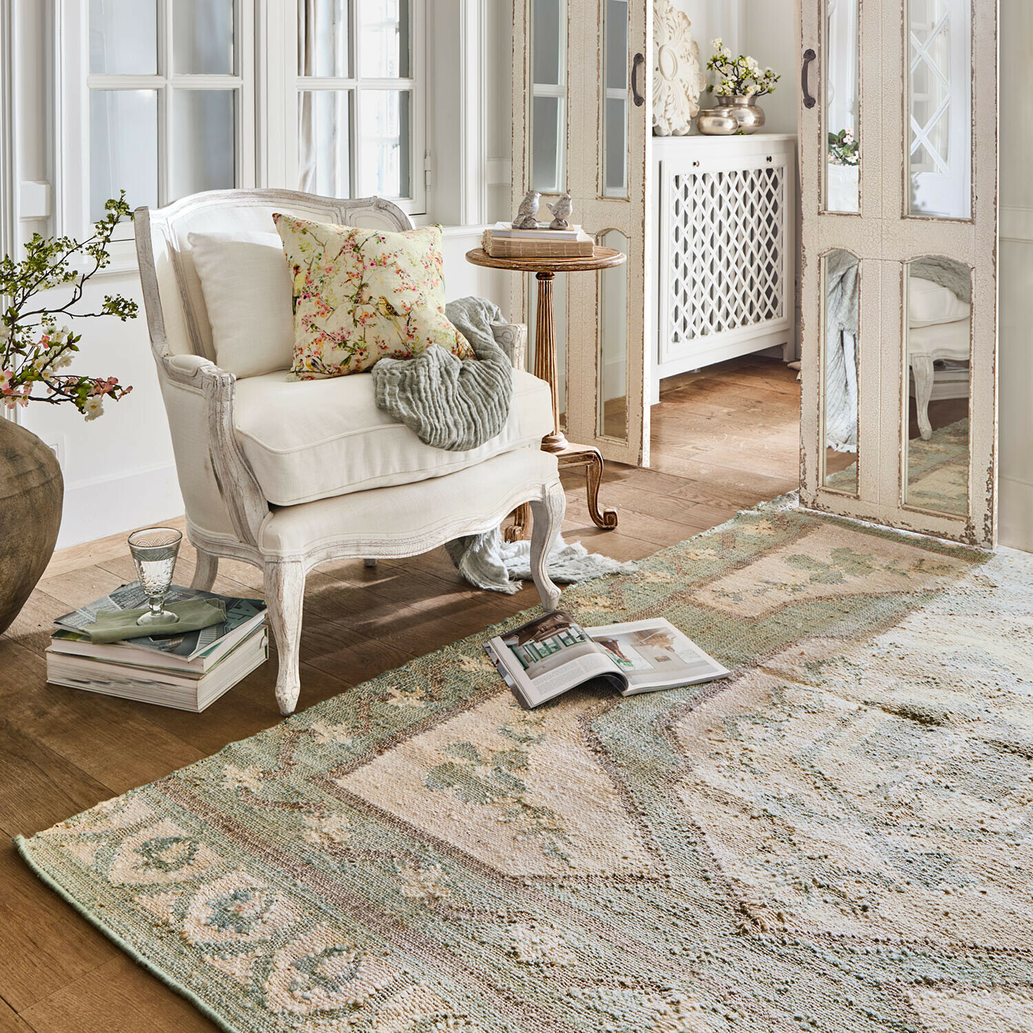 Vloerkleed Raneema Gezellige witte houten fauteuil met bloemkussen in lichte kamer met vintage vloerkleed in zachte kleuren