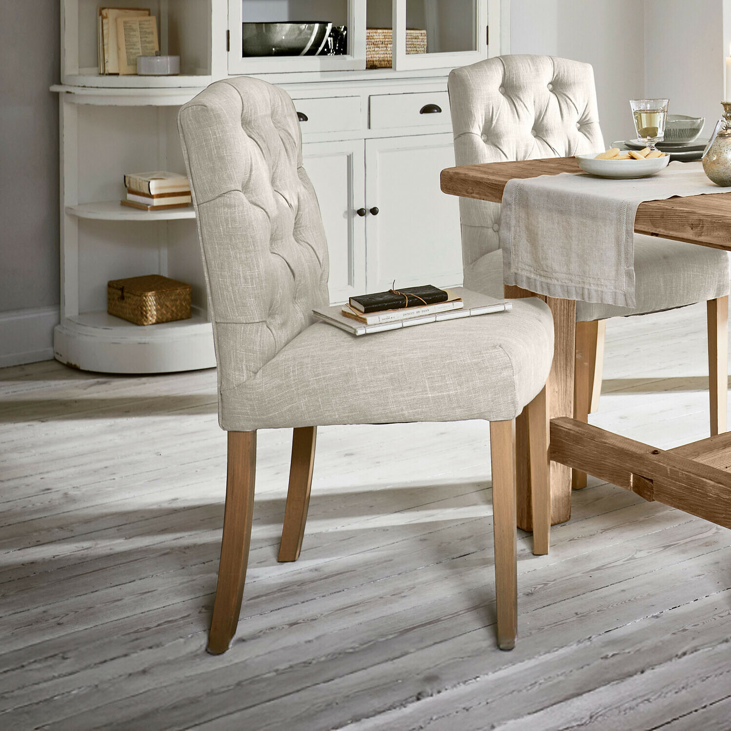 Stoel Fulden Beige gestoffeerde stoel met houten poten bij houten tafel in lichte kamer