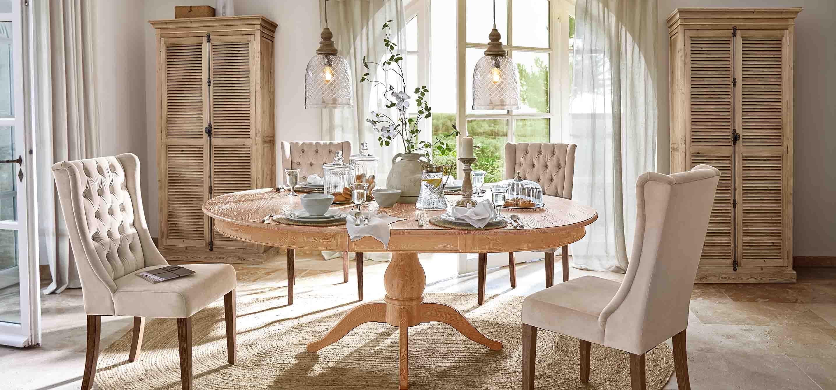 Eetkamer met ronde tafel van licht hout en beige gestoffeerde stoelen in vintage stijl