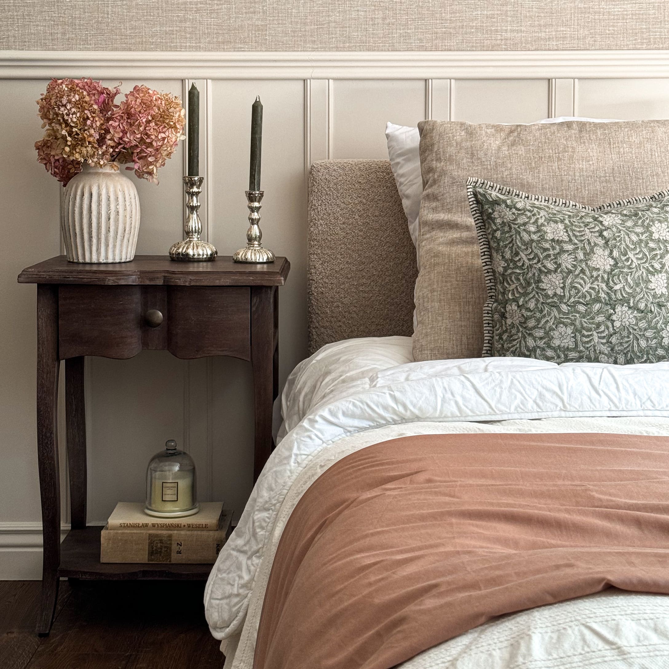 Chambre cosy avec literie beige, coussin vert et table de chevet en bois avec décorations élégantes