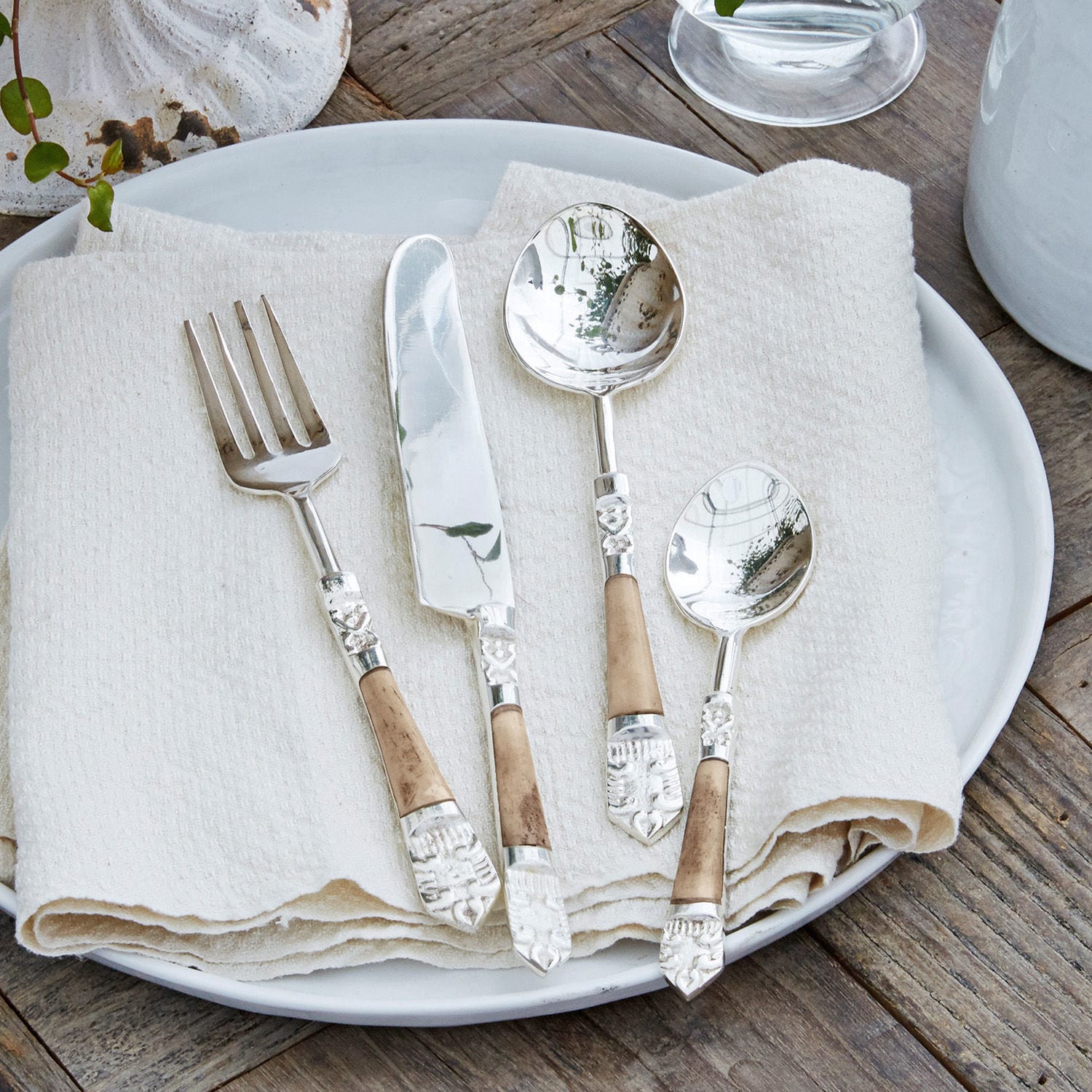 Lot de 4 couverts Ferrette Ensemble de couverts en métal avec manches en bois sur une assiette blanche avec serviette en lin