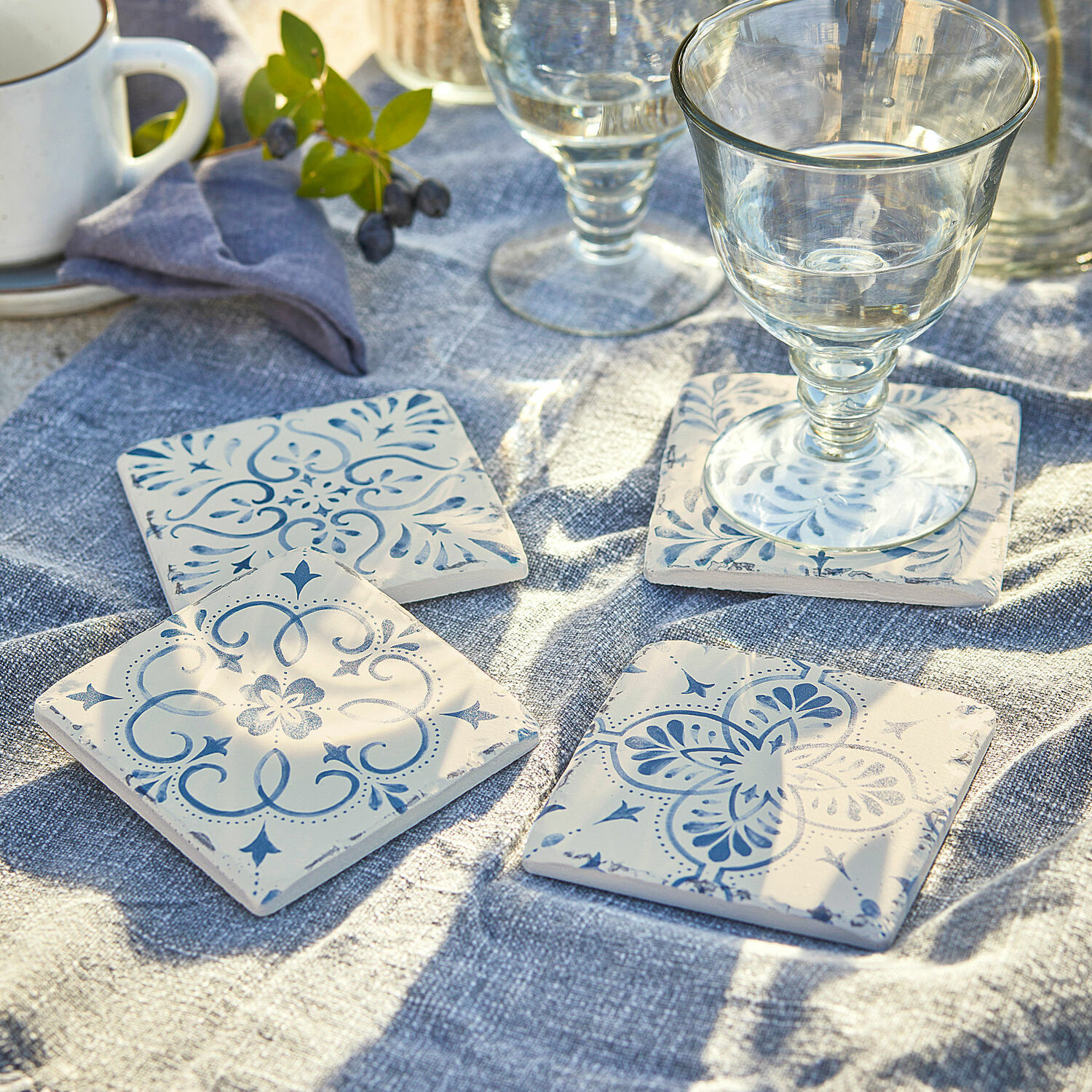 Lot de 4 dessous de verres Évry Dessous de verre en céramique blanche avec motifs bleus posés sur une nappe en lin bleu