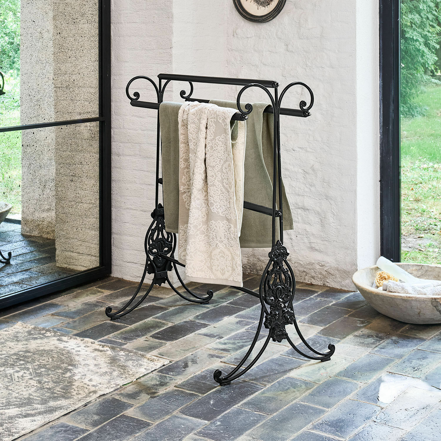 Porte-serviettes Tovrik Porte-serviettes en métal noir avec détails décoratifs sur sol en pierre dans un intérieur lumineux