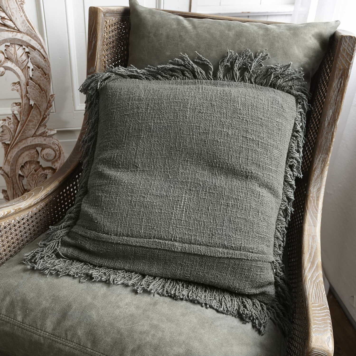 Coussin vert avec franges sur fauteuil en bois et rotin pour décoration intérieure