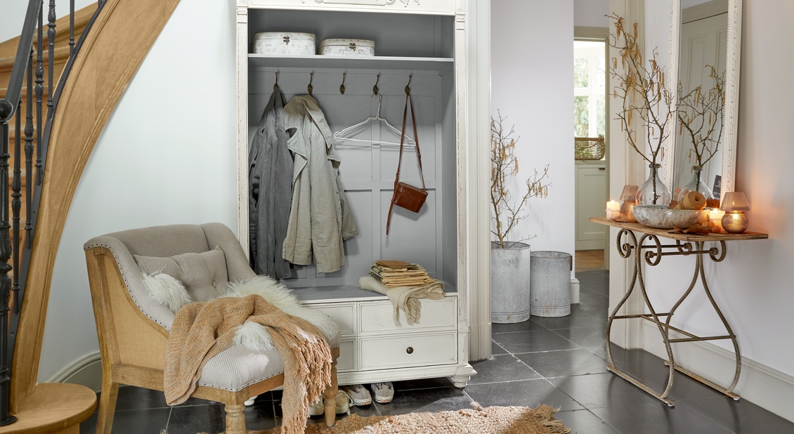 Gezellige hal met witte houten kast en beige vintage fauteuil op donkere vloer