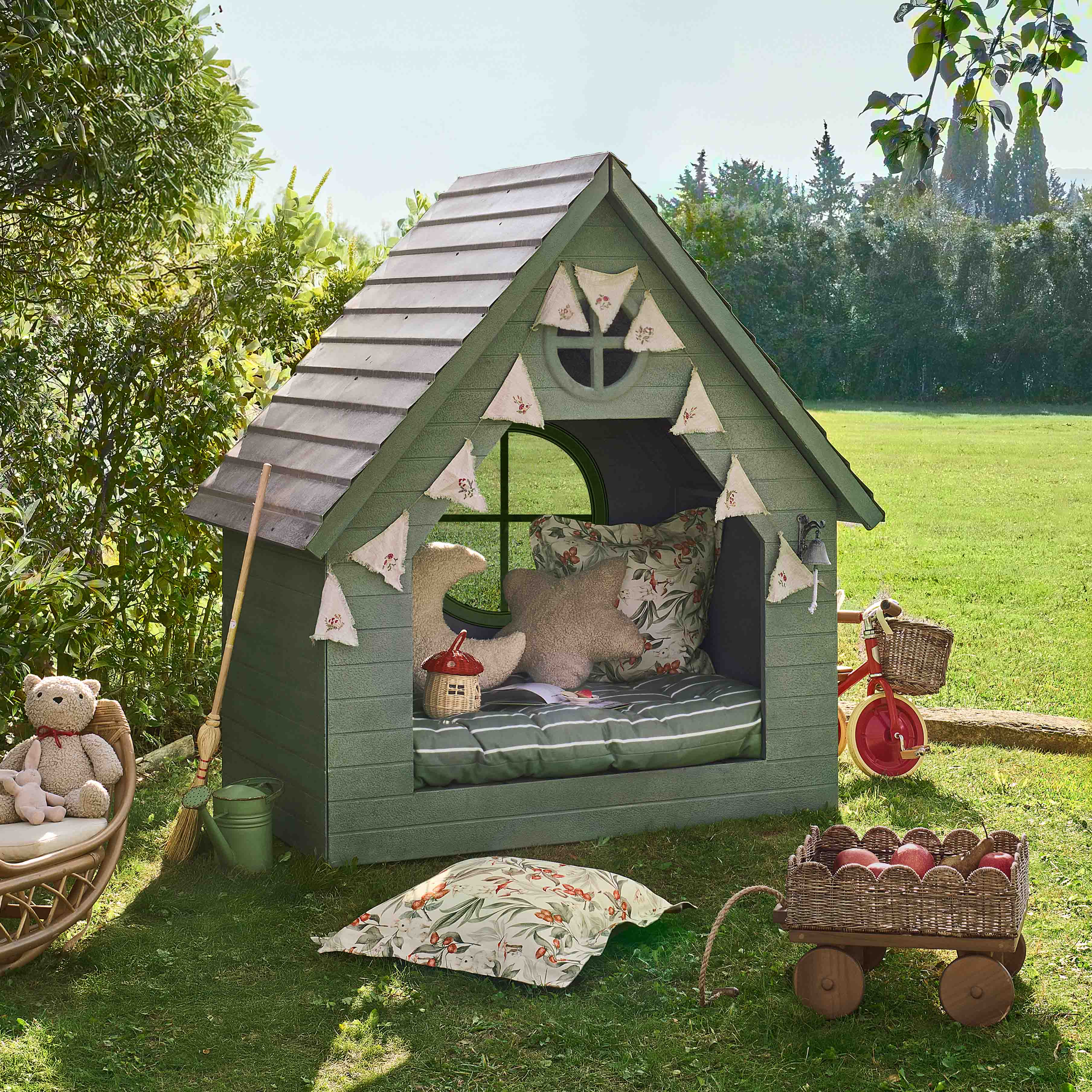 Maisonnette de jardin verte en bois avec coussins décoratifs et guirlande, parfaite pour les enfants.