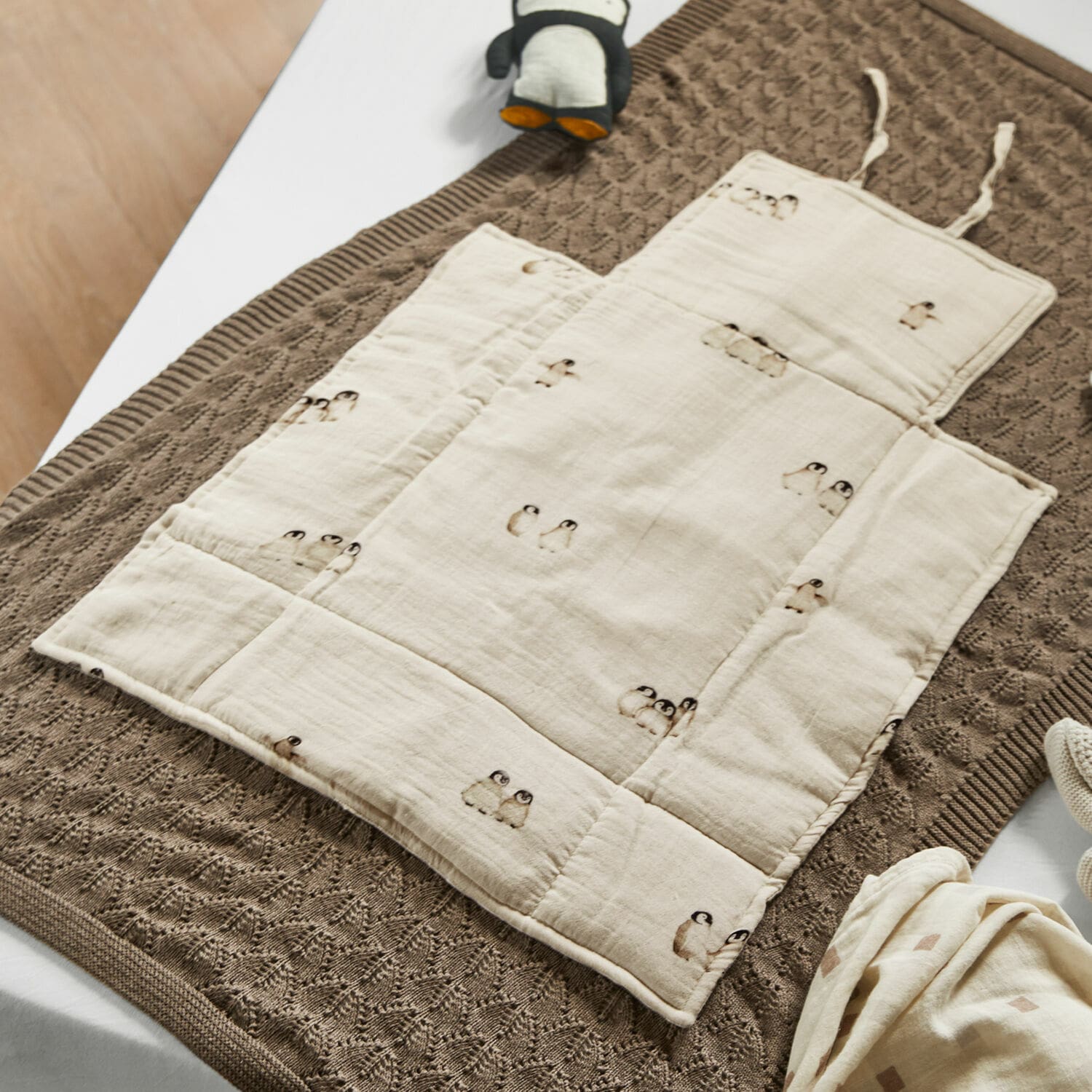 Verschoonkleed Jocienne Beige katoenen baby speelmat met pinguïnprint op bruine gebreide deken, babyaccessoires