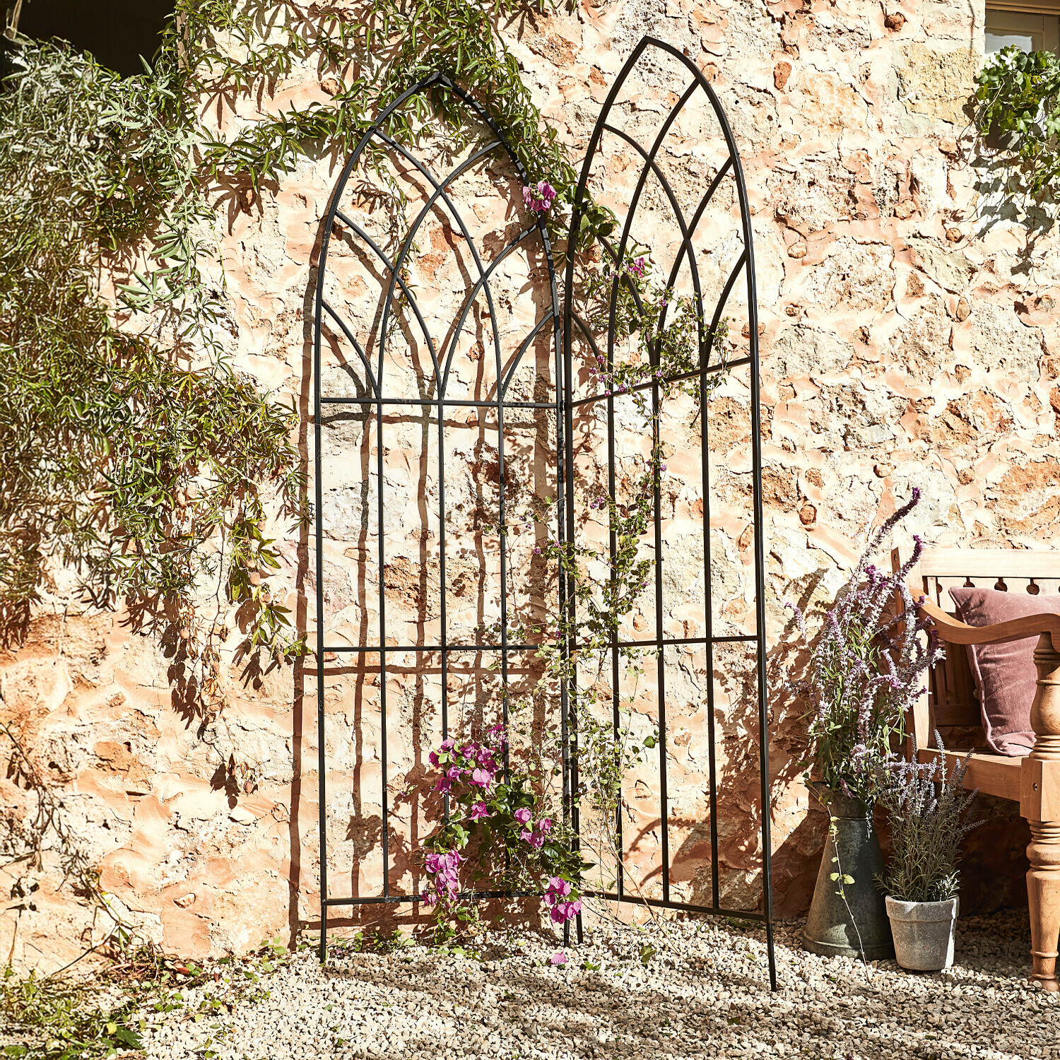 Treillis Ophélie Treillis de jardin en métal noir avec motif en arc devant un mur en pierre avec plantes grimpantes