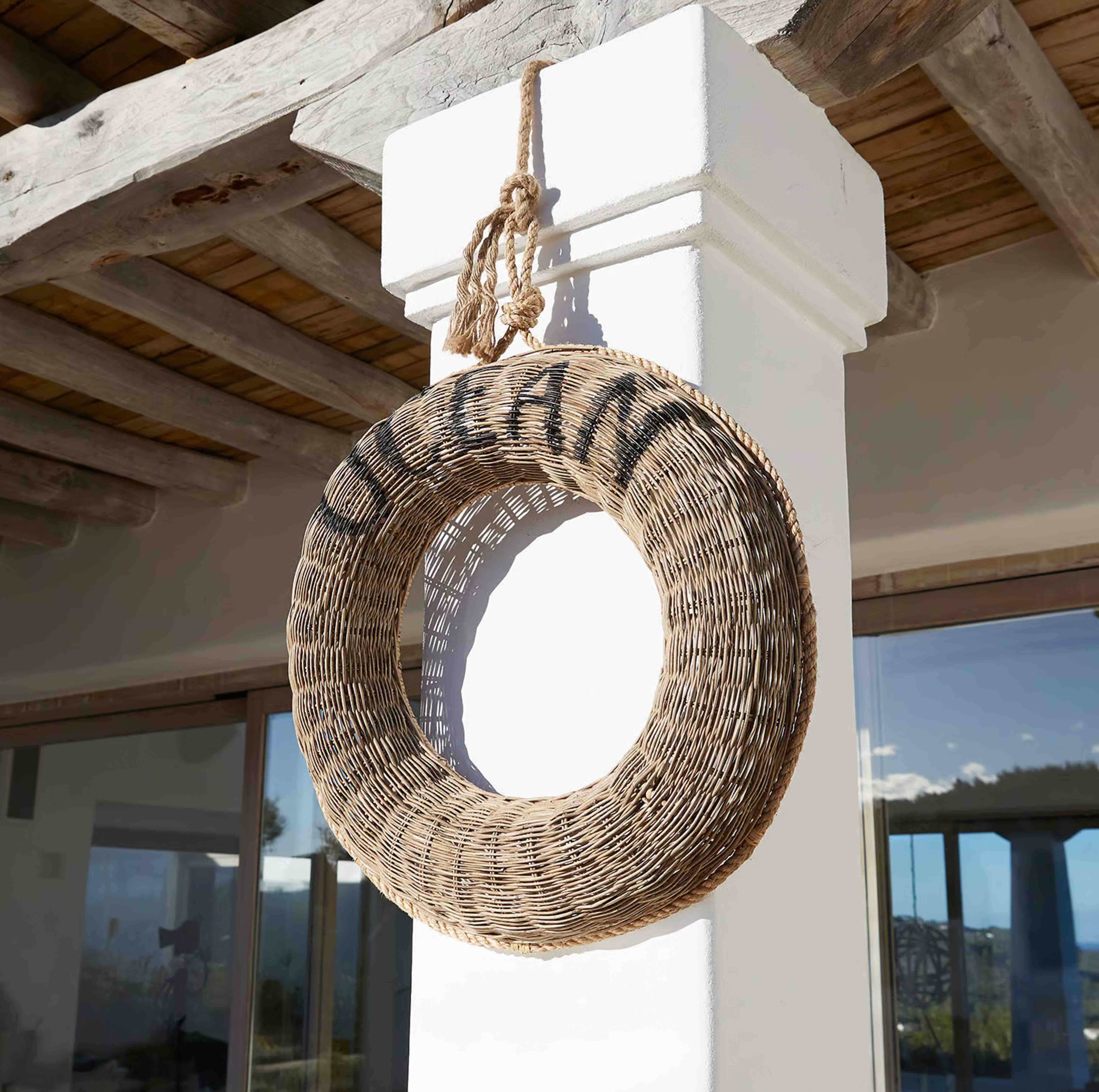 Couronne ronde en osier naturel suspendue à une colonne blanche sous un plafond en bois rustique