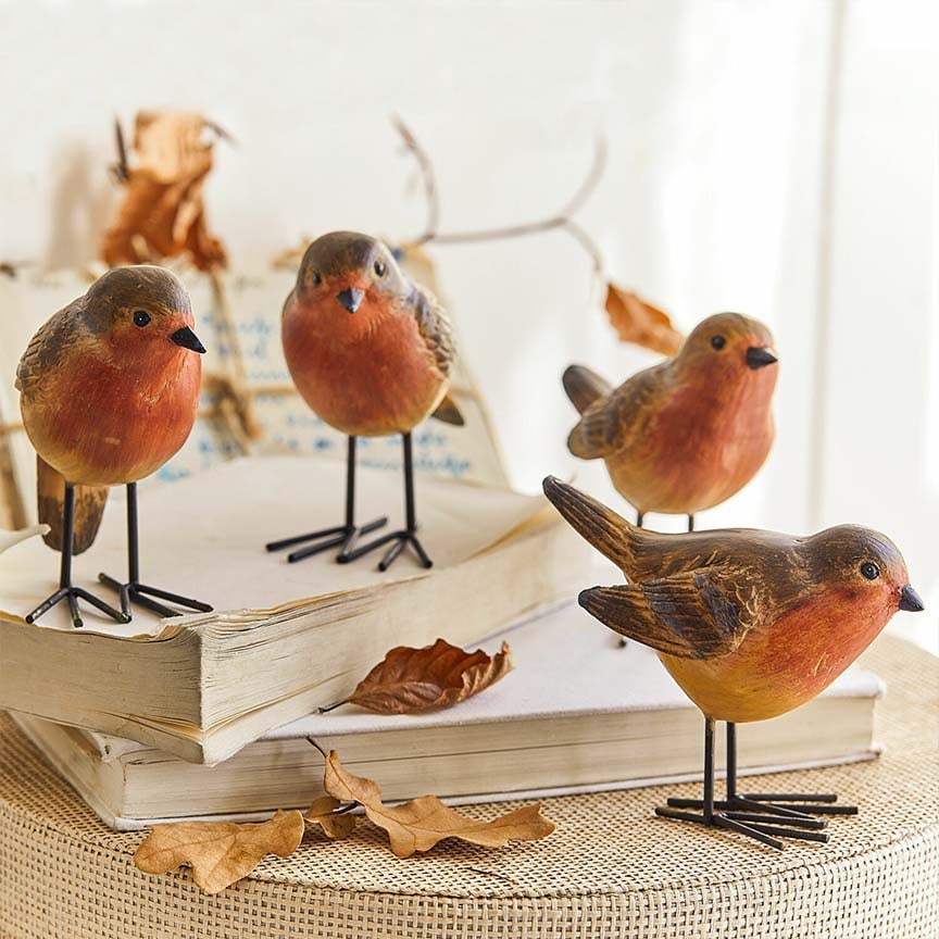 Decoratieve houten vogelbeeldjes in warme oranje- en bruintinten op boeken met droge bladeren