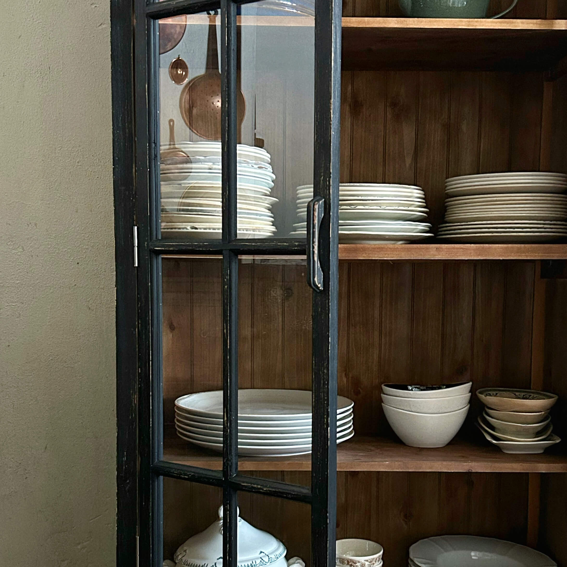 Zwarte houten kastdeur met glas, binnen witte borden en kommen op houten planken