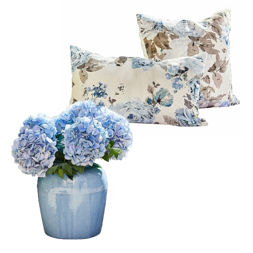 Hortensias bleus dans un vase en céramique bleue avec deux coussins à motif floral