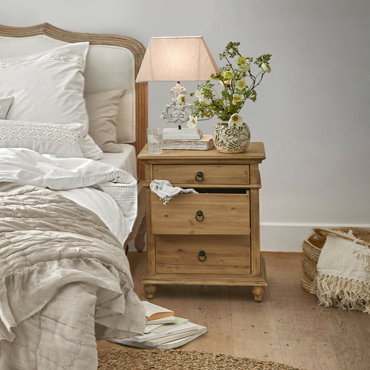 Houten nachtkastje met drie lades in natuurlijke kleur naast bed met wit beddengoed