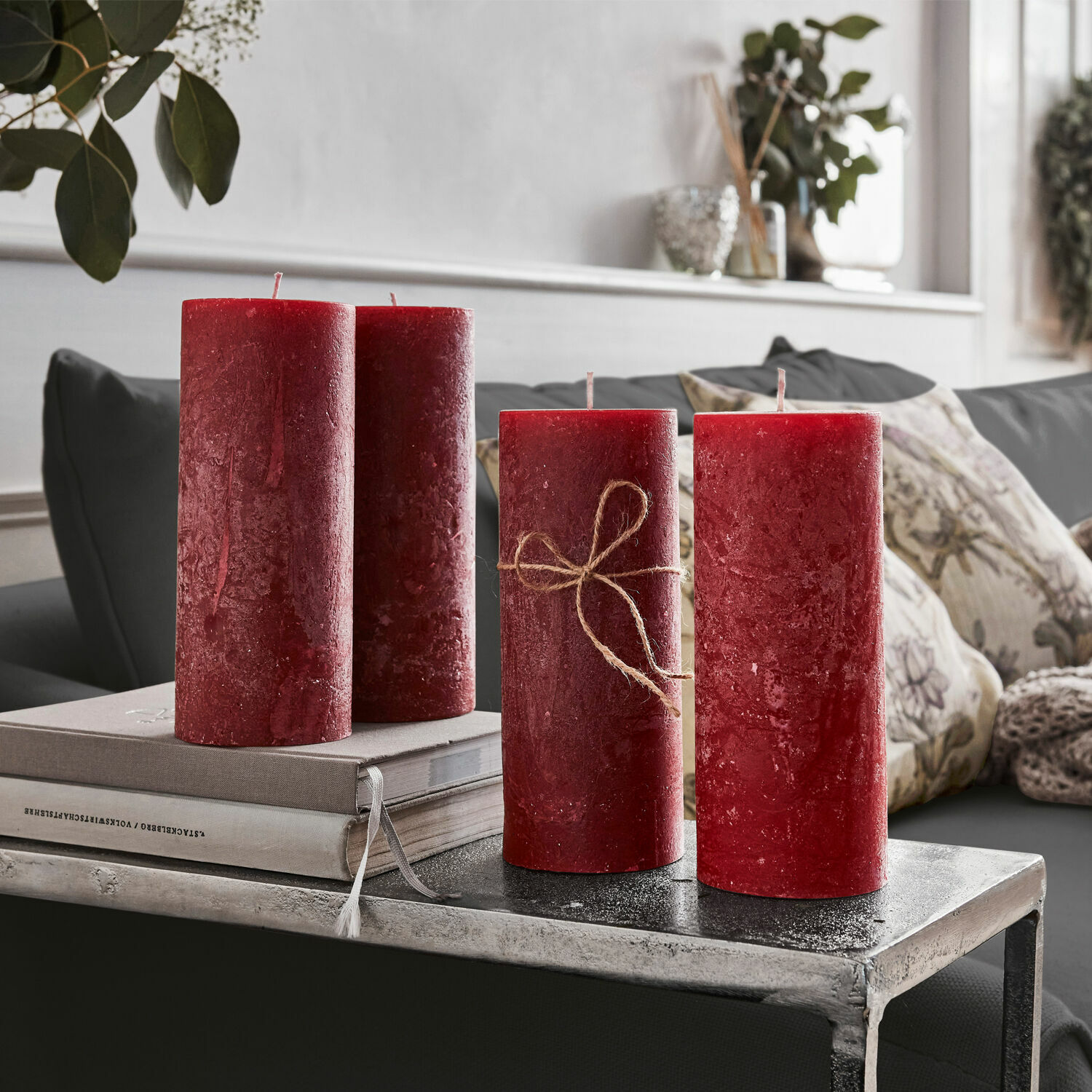 Lot de 4 bougies Homel Quatre bougies rouges en cire décoratives sur une table en métal dans un salon avec coussins