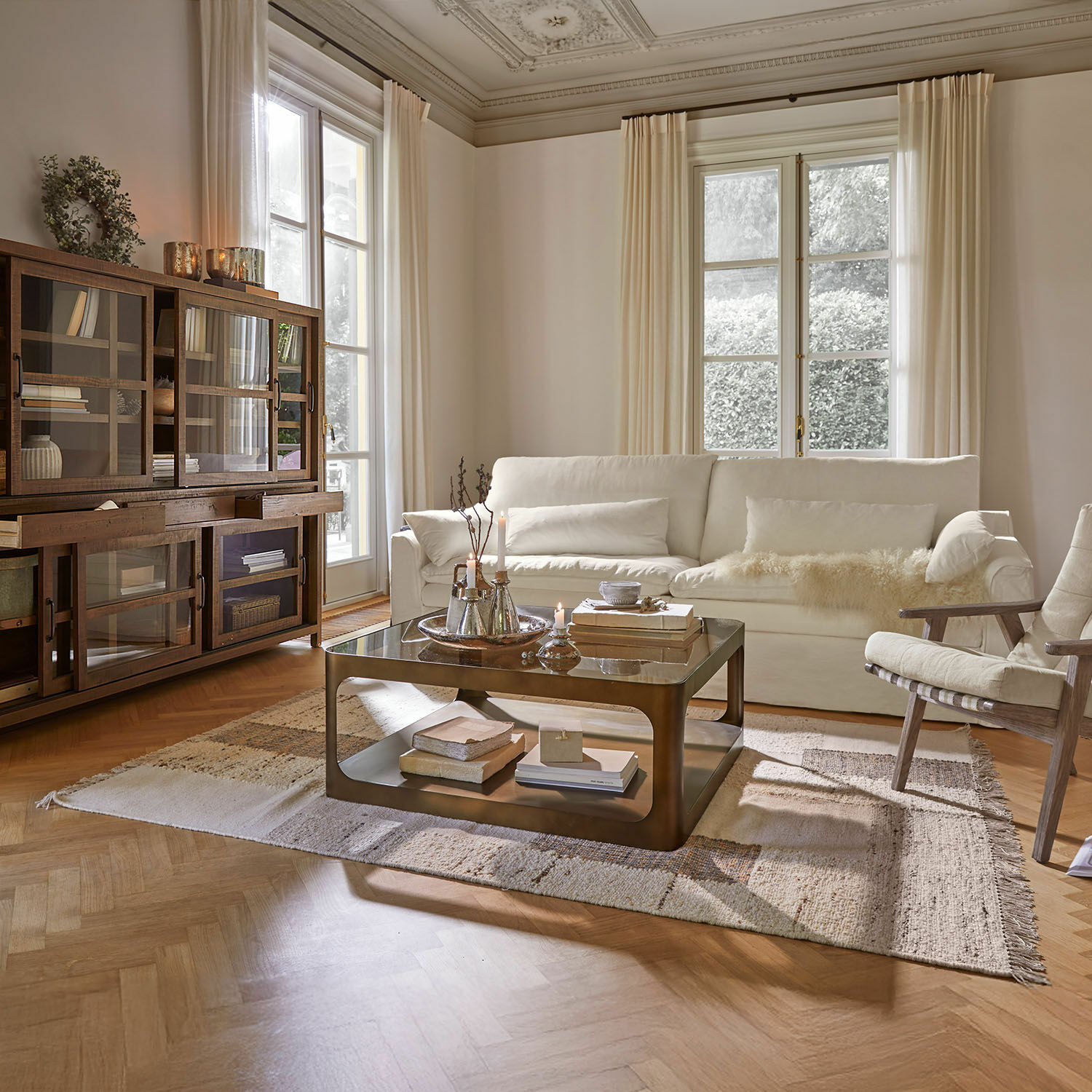 Gezellige woonkamer met witte bank, houten vitrinekast en metalen salontafel op vloerkleed