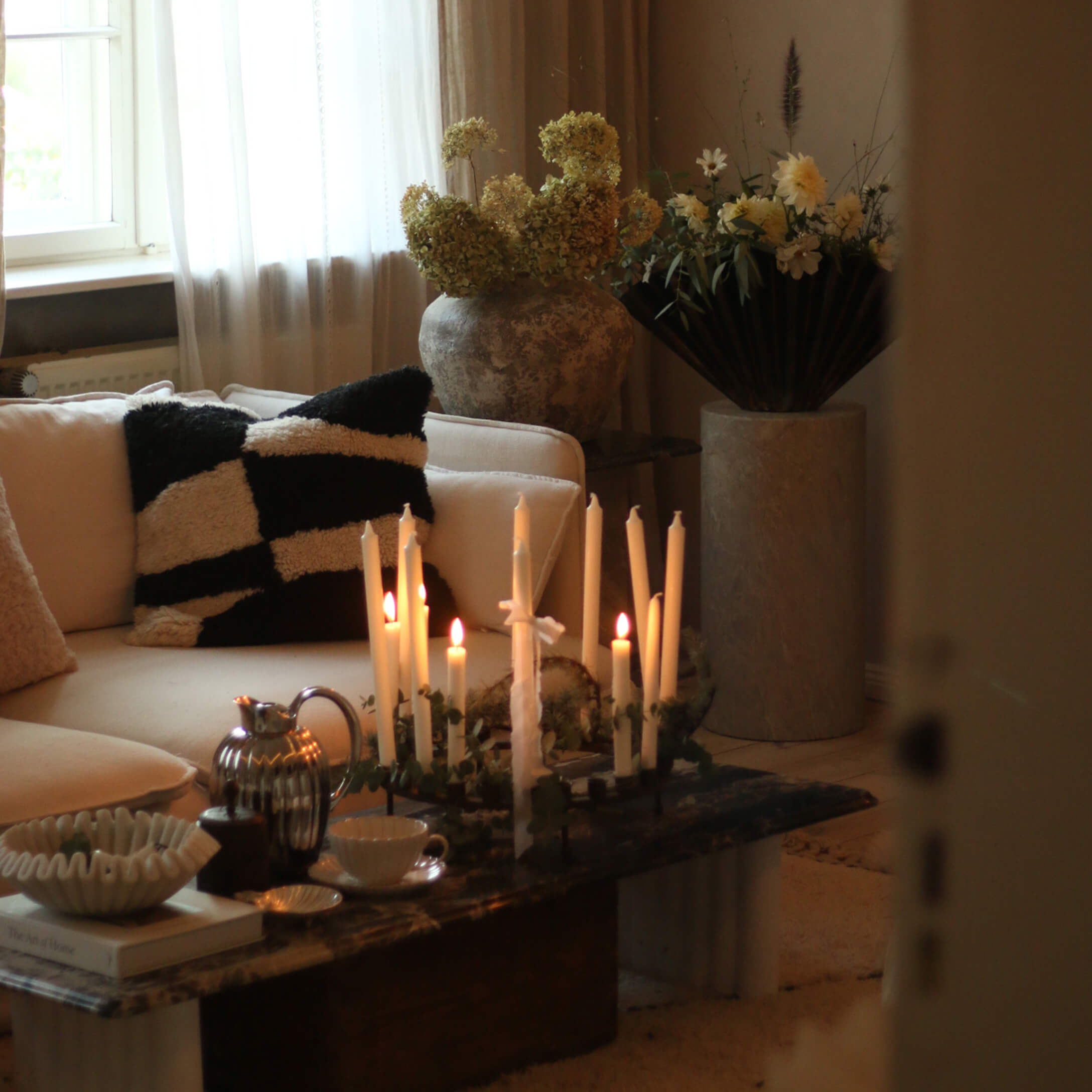 Salon chaleureux avec canapé crème, coussin noir et blanc et bougies allumées sur table en marbre
