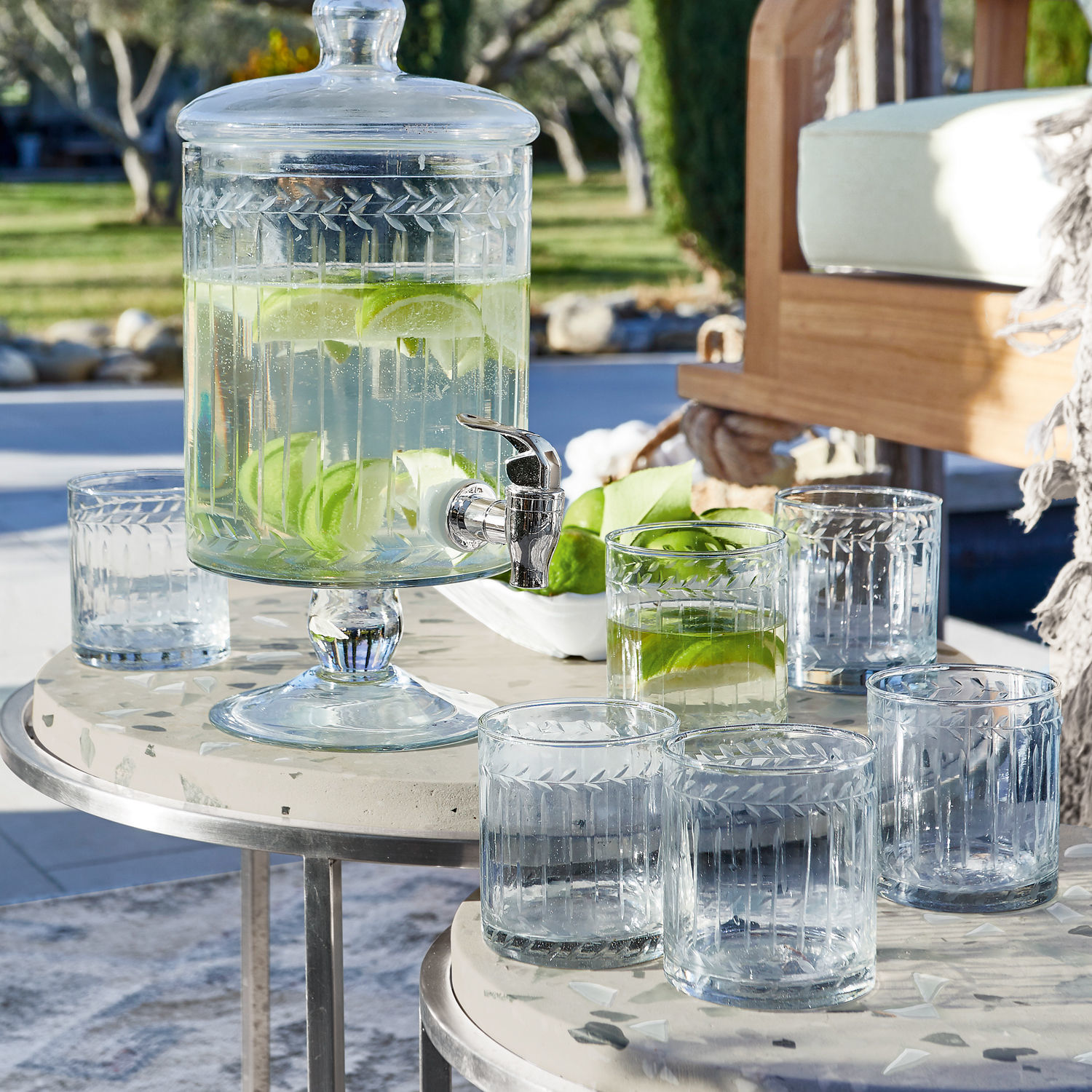 Glas set van 6 Padiès Glazen drankdispenser met deksel en kraan, gevuld met water en limoenpartjes op een terras