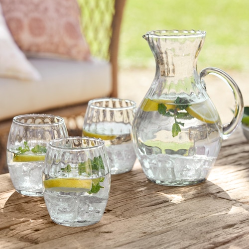 Carafe en verre et trois verres avec eau, citron et menthe sur table en bois en extérieur