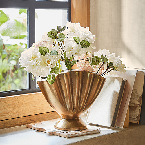 Vase décoratif en métal doré avec fleurs blanches sur rebord de fenêtre, décoration intérieure élégante