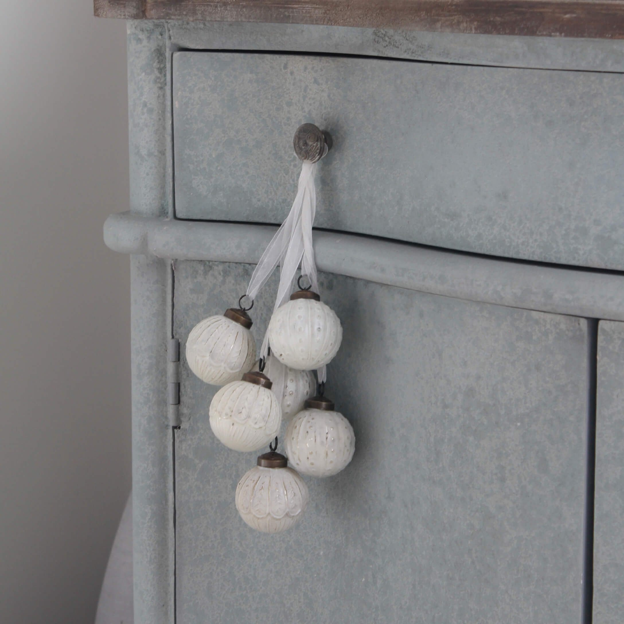 Ensemble de boules décoratives blanches avec motifs suspendues à un meuble en métal gris