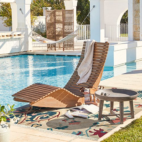 Chaise longue en bois sur terrasse au bord de la piscine avec tapis coloré et table basse