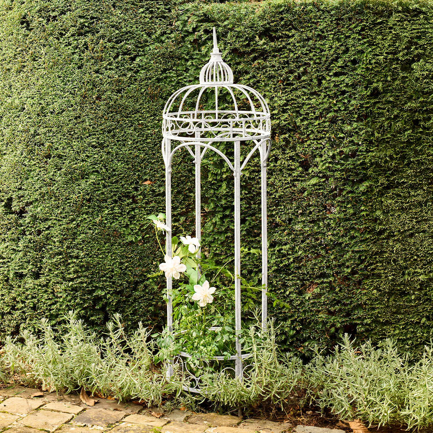 Witte metalen tuinprieel met decoratief patroon, die klimplanten ondersteunt voor een groene haag