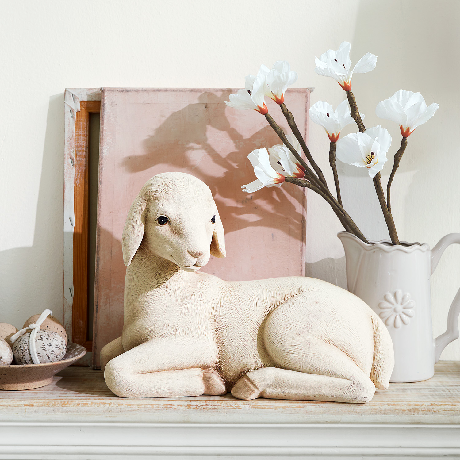 Figurine décorative de mouton beige posée sur une étagère en bois avec fleurs blanches