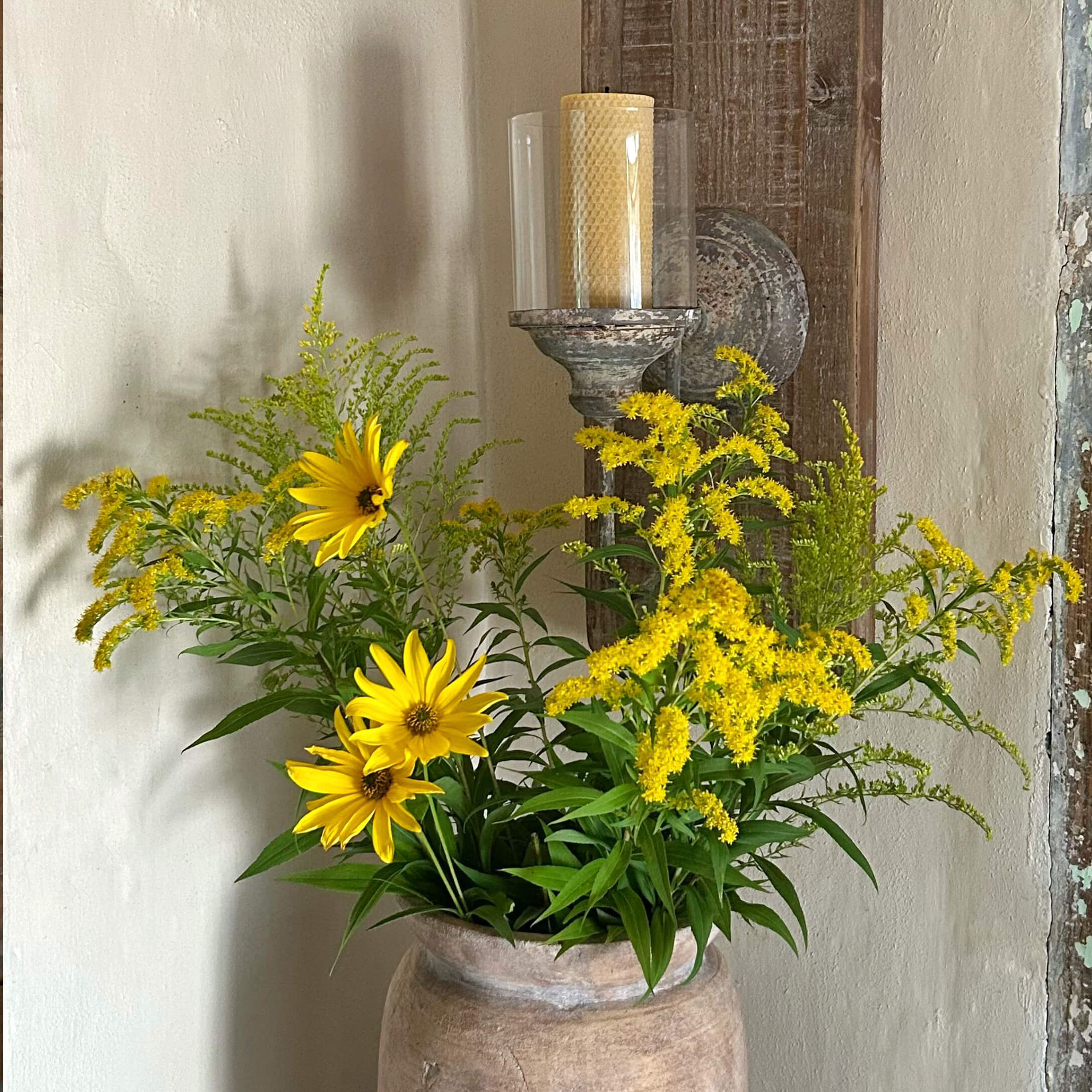 Fleurs jaunes dans un vase en terre cuite devant un mur avec un bougeoir rustique