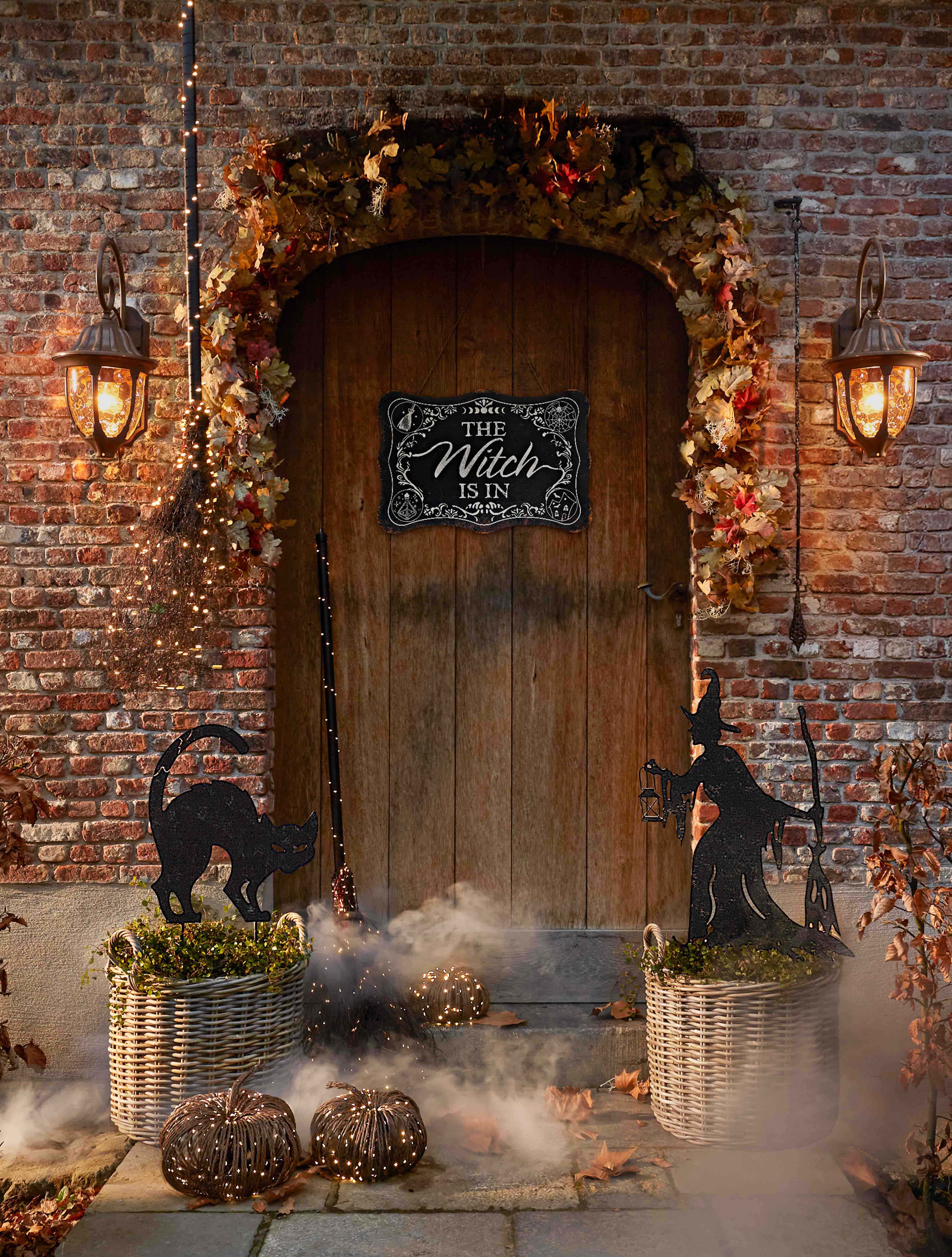 Halloweenversiering met heks, zwarte kat en lantaarns bij houten deur en bakstenen muur