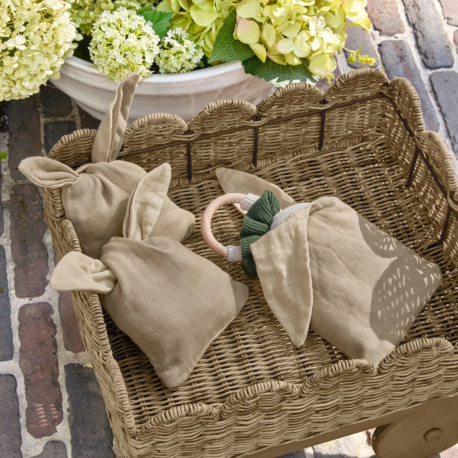 Set de 3 sacs Snugglewood Sac en lin beige avec oreilles dans un panier en osier, décor floral et sol en briques