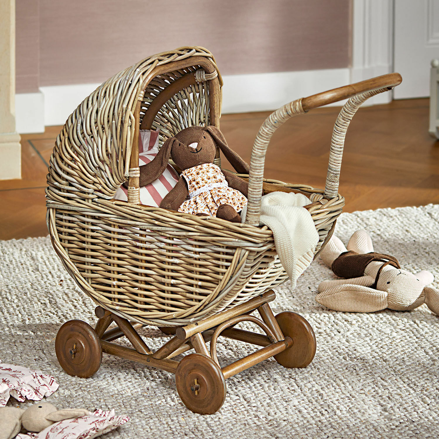 Poussette de poupée Fableton Poussette en osier avec roues en bois et peluches, posée sur un tapis dans une chambre d'enfant