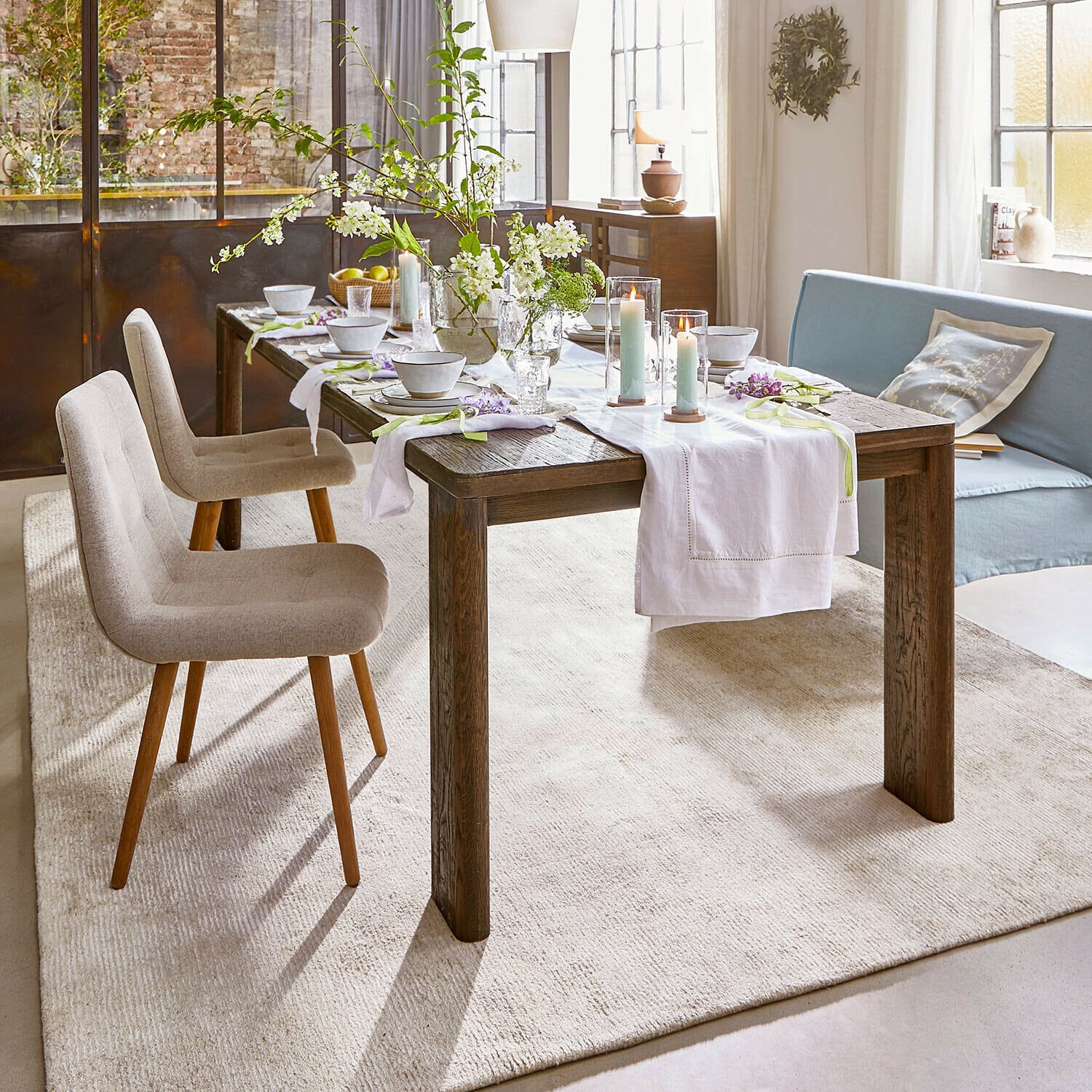 Tafel Gianoro Rustieke eettafel van donker hout met wit tafelkleed en kaarsen in lichte woonkamer