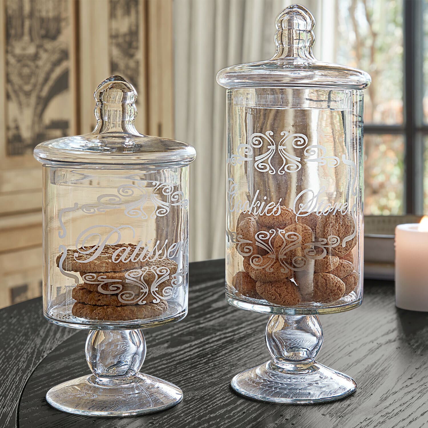 Lot de 2 bonbonnières Suzie Bocaux en verre avec couvercles et inscriptions décoratives remplis de biscuits sur une table noire