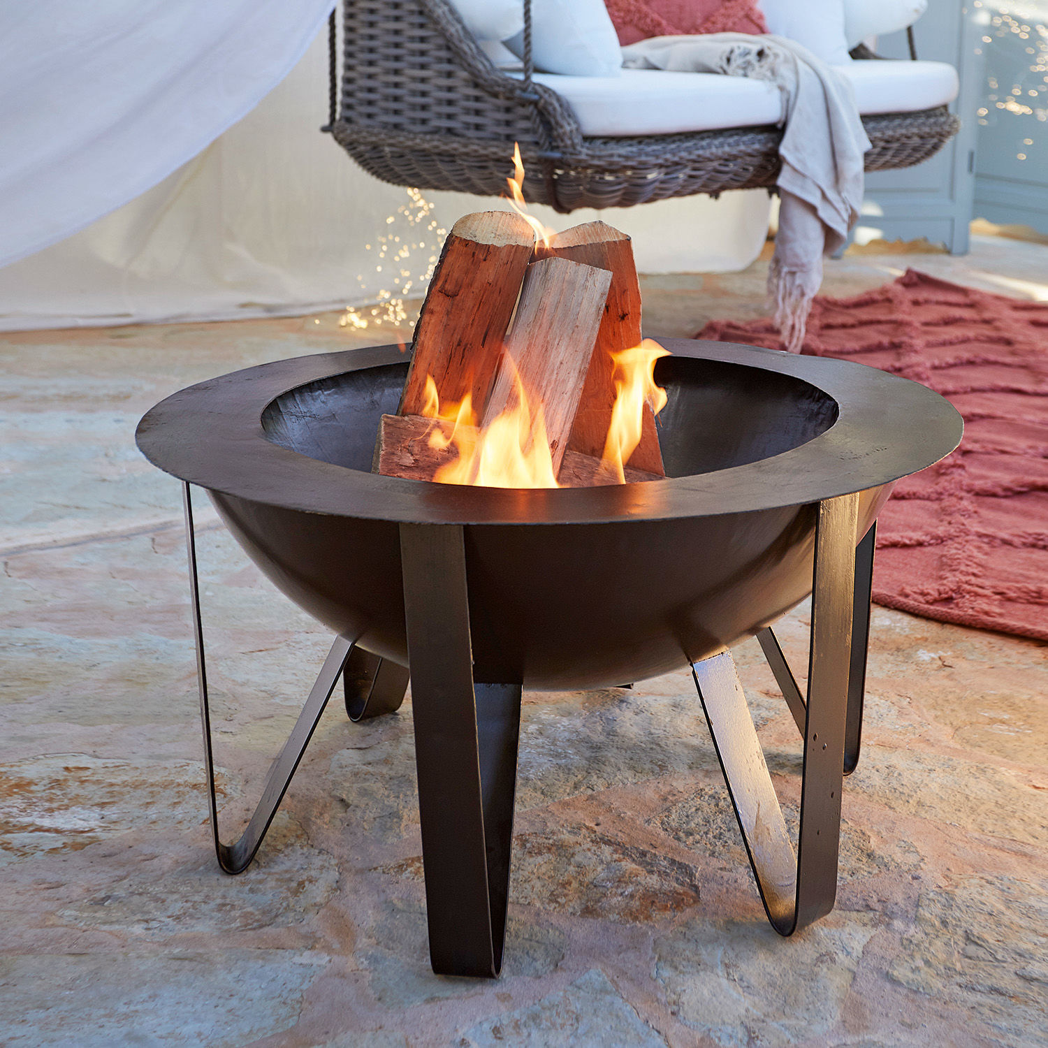 Brasero Lovis Brasero en métal noir avec bois en feu sur sol en pierre dans un intérieur chaleureux