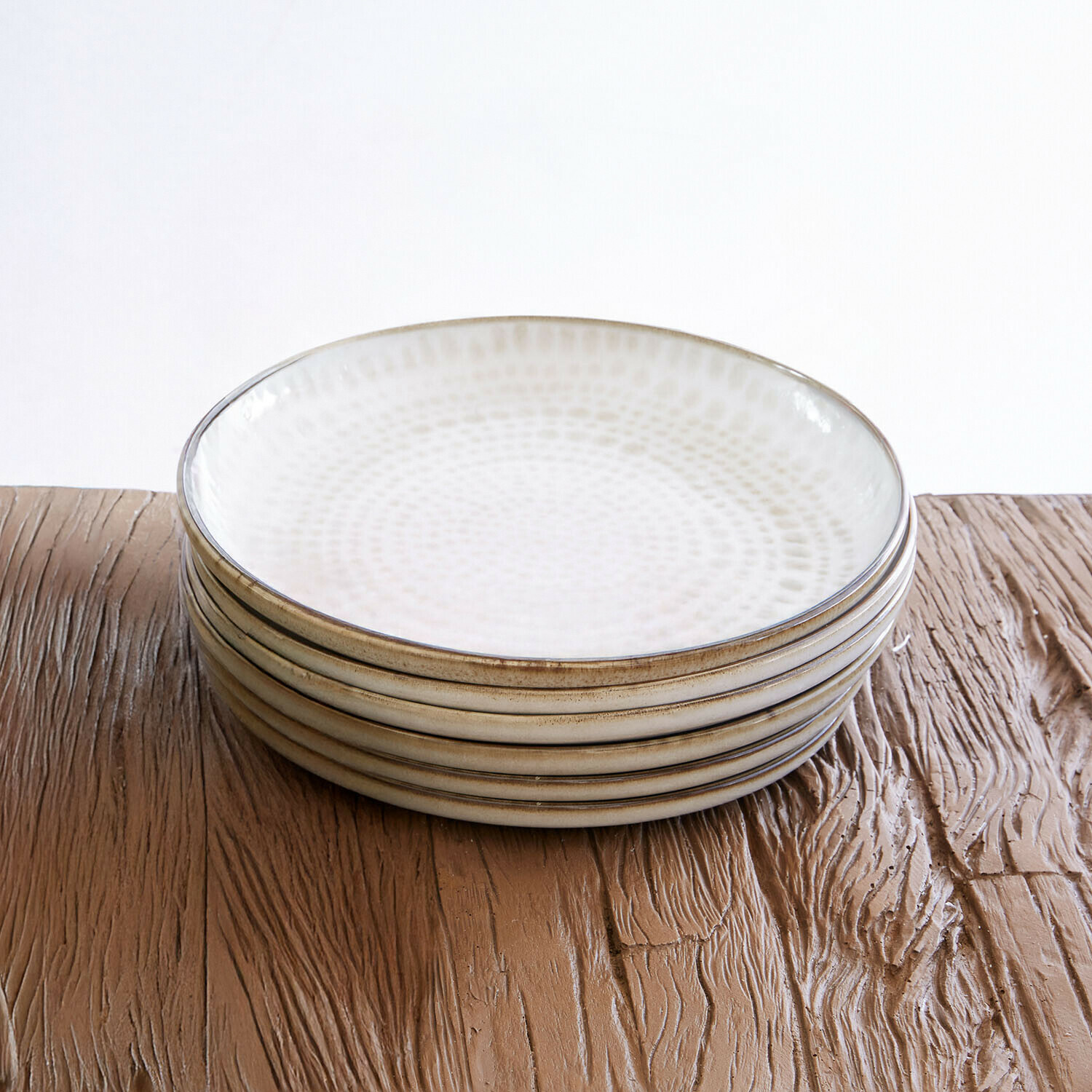 Lot de 6 assiettes Marnis Ensemble de six assiettes en céramique crème avec motif subtil, posées sur une table en bois