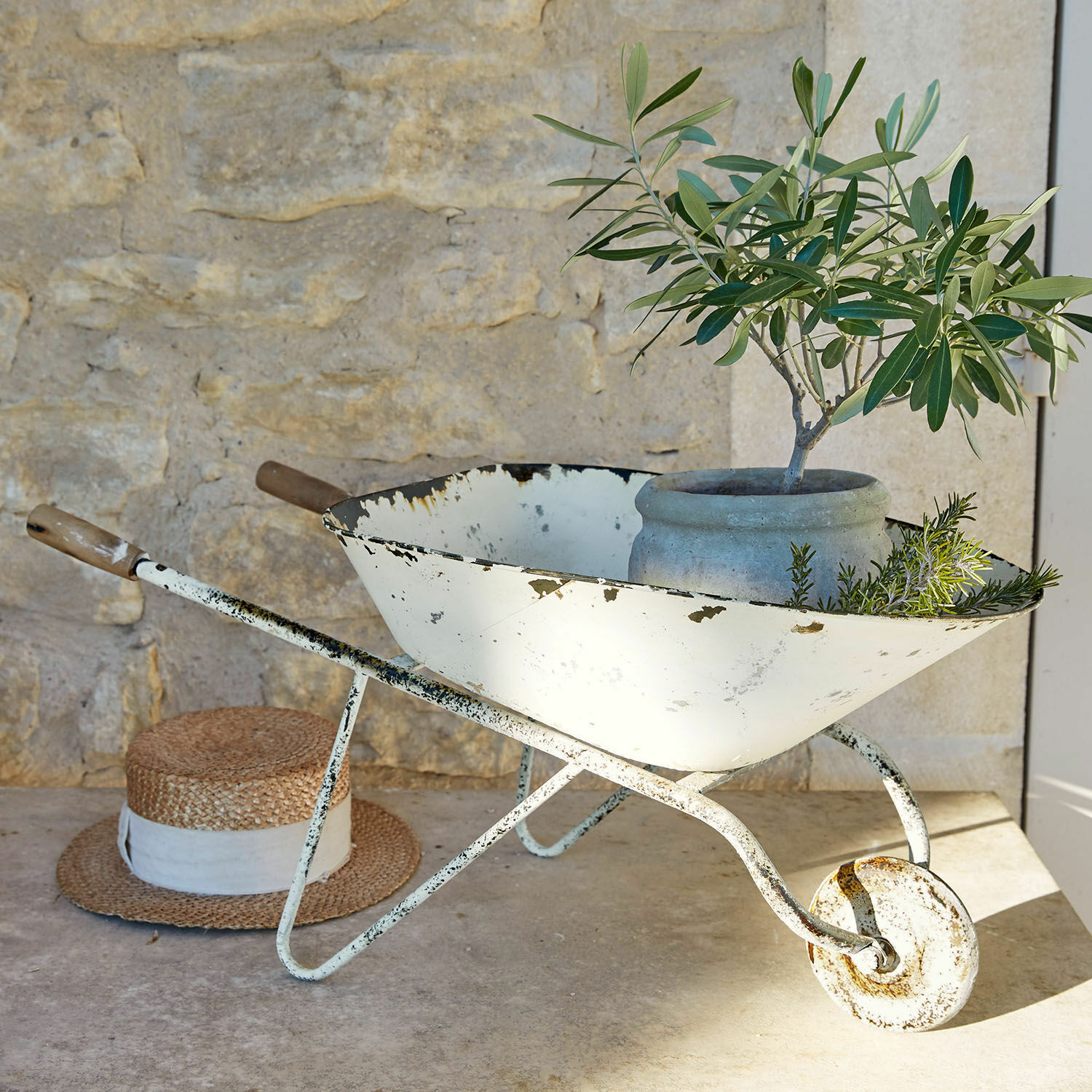 Sierkruiwagen Padoux Witte metalen kruiwagen met verweerde look, pot en groene planten voor stenen muur