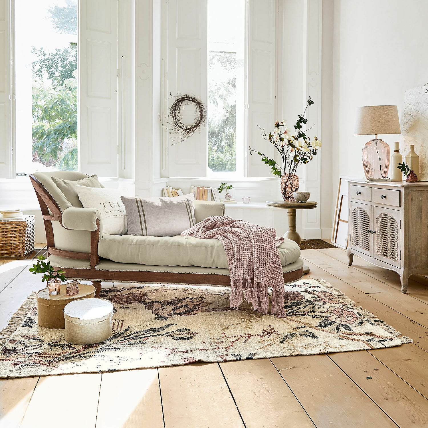 Beige gestoffeerde chaise longue met houten frame en roze deken in lichte woonkamer met vloerkleed