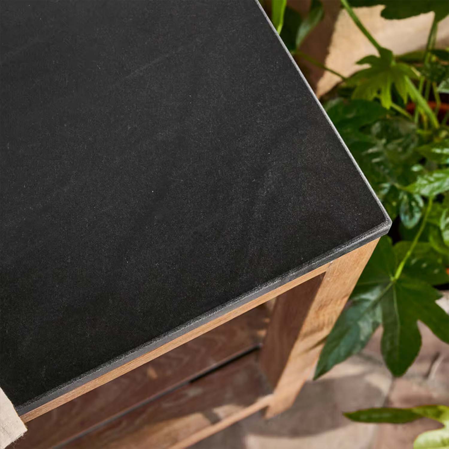 Plateau de table en pierre noire avec base en bois entouré de plantes vertes, mobilier d'extérieur