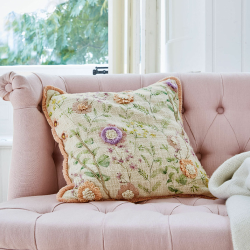 Decoratief kussen met bloemenborduursel in pasteltinten op roze bank, zacht materiaal