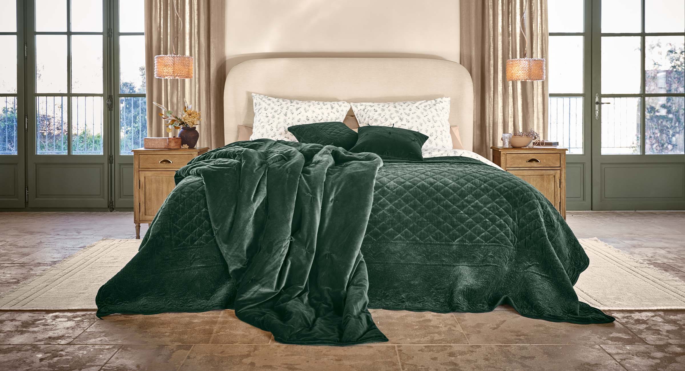 Chambre confortable avec lit et couverture en velours vert foncé avec coussins assortis