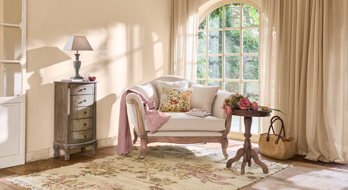 Salon chaleureux avec canapé beige, plaid rose et table en bois avec fleurs, lumière naturelle douce