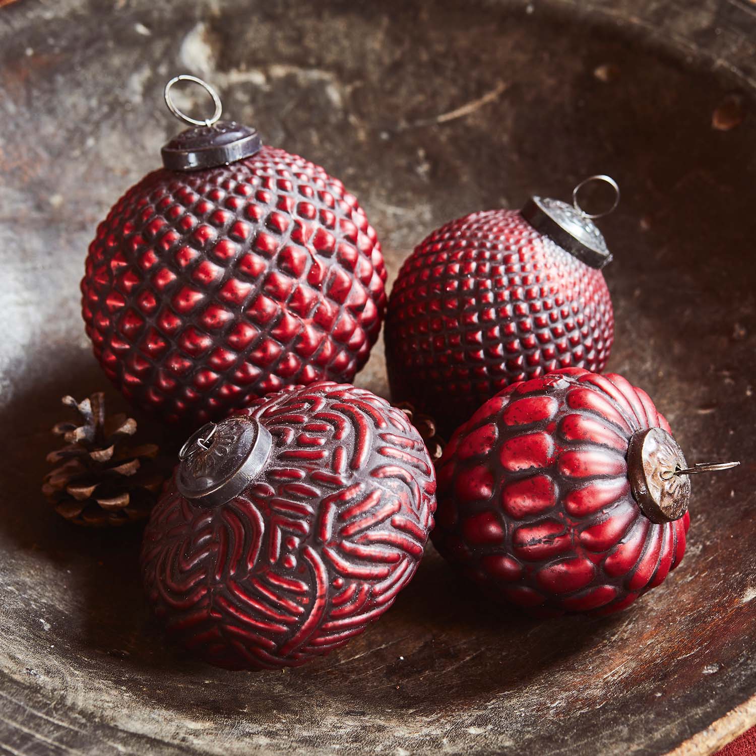 Quatre boules de Noël rouges texturées posées dans un bol en bois avec des pommes de pin