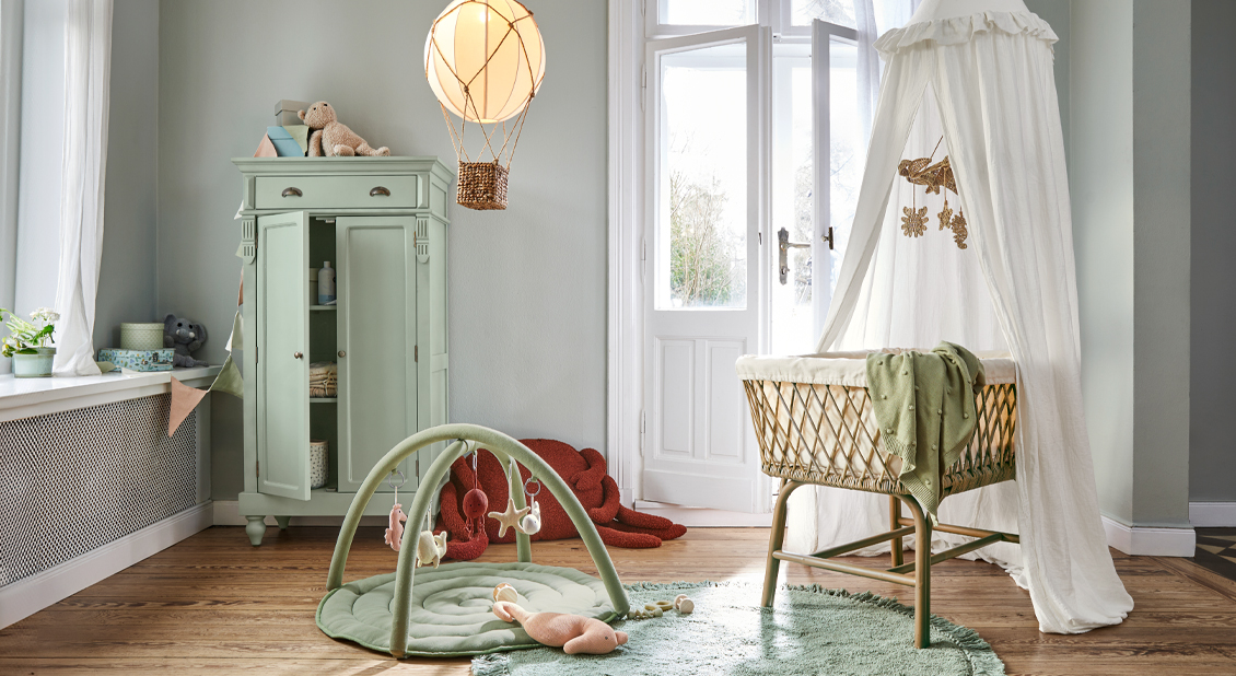 Gezellige babykamer met rotan wieg, groene vloerkleed en pastelgroene kast, zachte lichte inrichting
