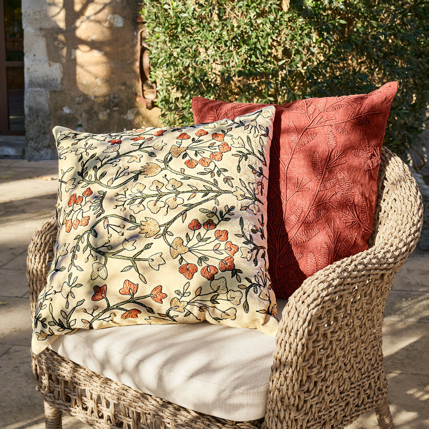 Twee decoratieve kussens met bloemen- en bladborduursel op een rotan stoel buiten