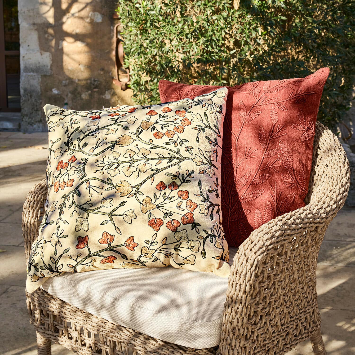 Lot de 2 housses de coussins Calévine Deux coussins décoratifs brodés de motifs floraux et feuillages sur fauteuil en osier en extérieur