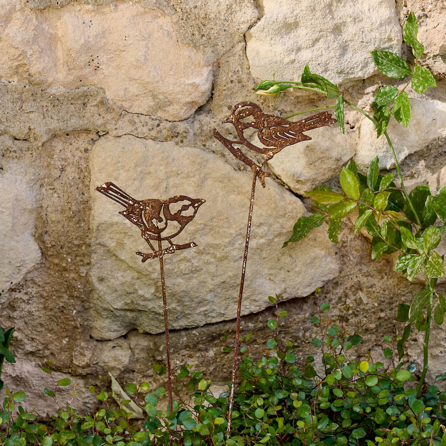 Lot de deux piques de jardin Pelvaron Décorations de jardin en métal rouillé en forme d'oiseaux sur tiges devant un mur en pierre