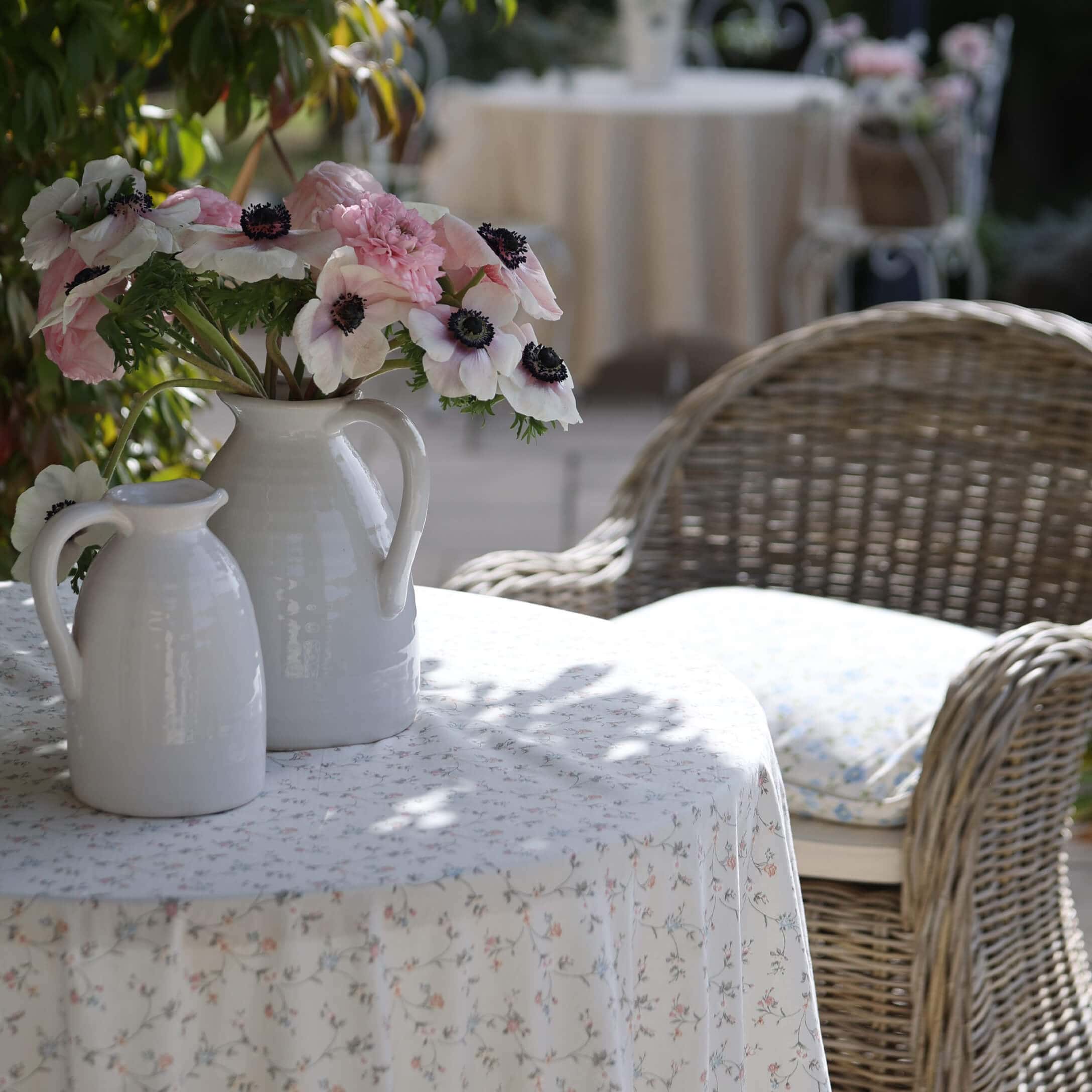 Carafes en céramique blanche avec fleurs roses et blanches sur une table à nappe fleurie en extérieur
