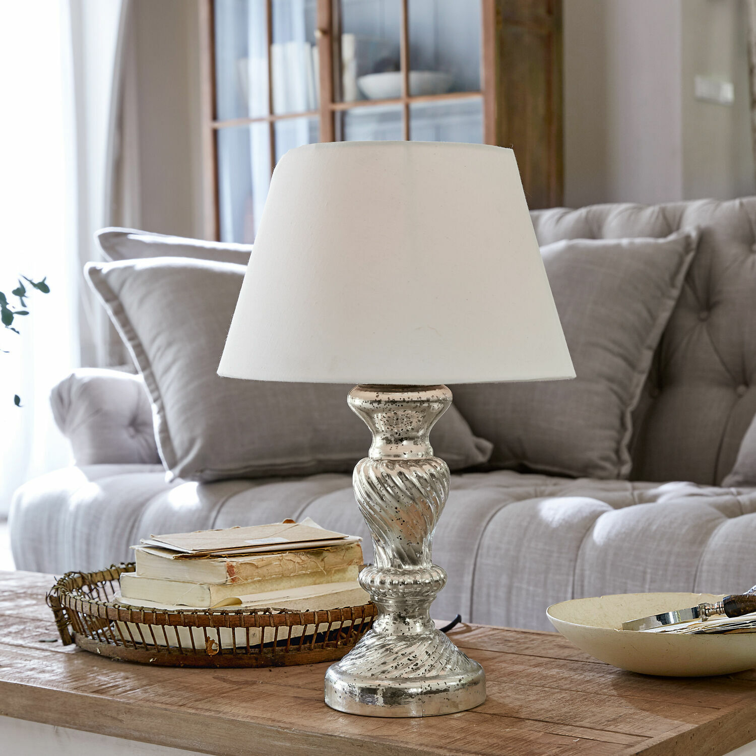 Lampe à poser Hazel Lampe de table avec abat-jour blanc et base argentée sur une table en bois dans un salon