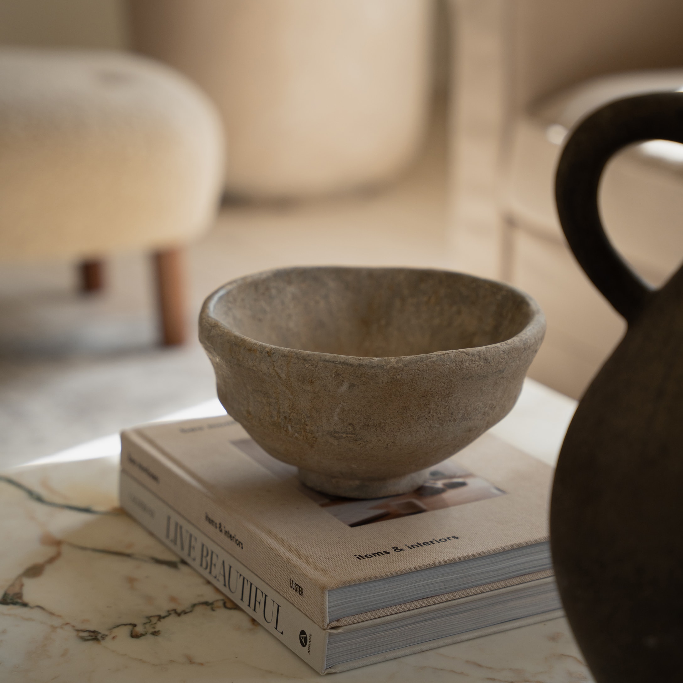 Decoratieve kom van natuurlijke beige steen op boek op marmeren tafel in gezellige ruimte